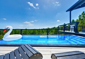 A swimming pool with a swan float, wooden deck, and a covered area with seating. - King Suite | Mtn Views | EV Charger | Heated Pool (Broken Bow)