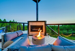 An outdoor deck with a built-in fire feature, seating, and a view of the surrounding landscape. - King Suite | Mtn Views | EV Charger | Heated Pool (Broken Bow)