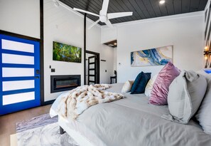 Un dormitorio moderno con cama, chimenea, ventilador de techo y obras de arte en las paredes.