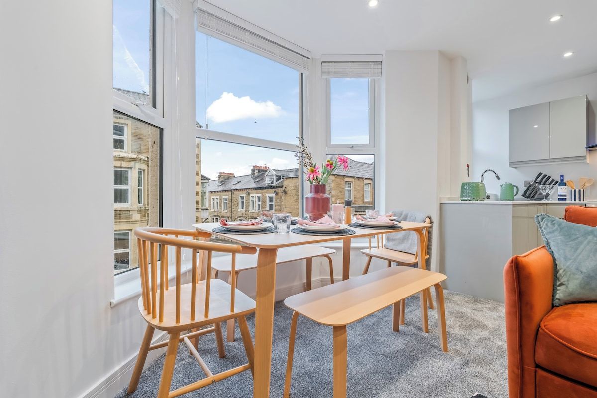 A modern kitchen with a dining area, large windows, and a view of the cityscape.
