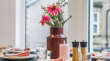 A dining table set with plates, glasses, and a centerpiece of pink flowers in a brown vase.