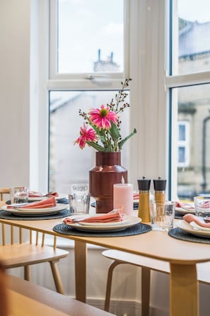 Mesa de comedor dispuesta con platos, vasos y un centro de mesa de flores rosadas en un jarrón marrón.