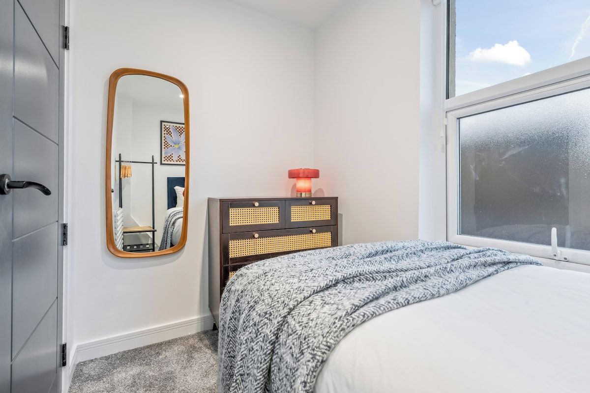 A bedroom with a bed, a dresser, a mirror, and a window.