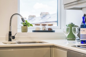 Una cocina con un grifo moderno, una planta en maceta, especias, un hervidor verde y copas de vino sobre la encimera.