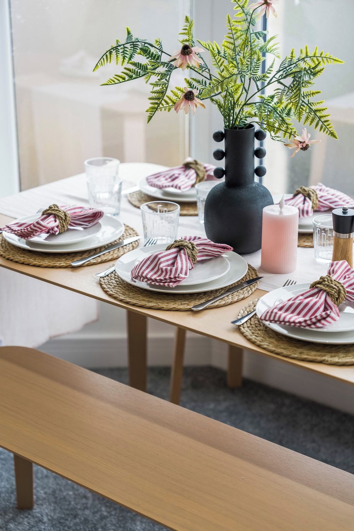 Une table à manger dressée avec des assiettes, des verres, une bougie et un vase contenant des plantes vertes.
