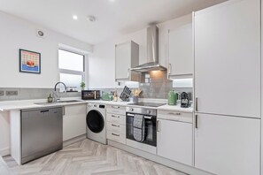 A modern kitchen with stainless steel appliances, a dishwasher, a washing machine, and a built-in oven. - Coastal retreat near Morecambe Bay and promenade (Heysham)