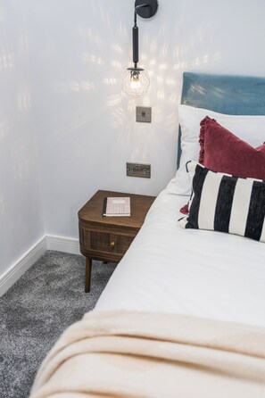 Cama bem arrumada com travesseiro listrado, abajur e mesa de cabeceira de madeira com um livro.