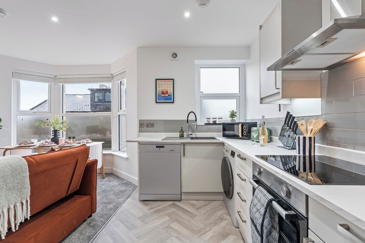 A modern kitchen with a dishwasher, oven, and a dining area with a sofa.
