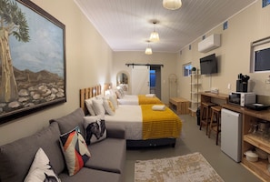A hotel room with a bed, a sofa, a desk with a computer, a TV, and a painting on the wall.