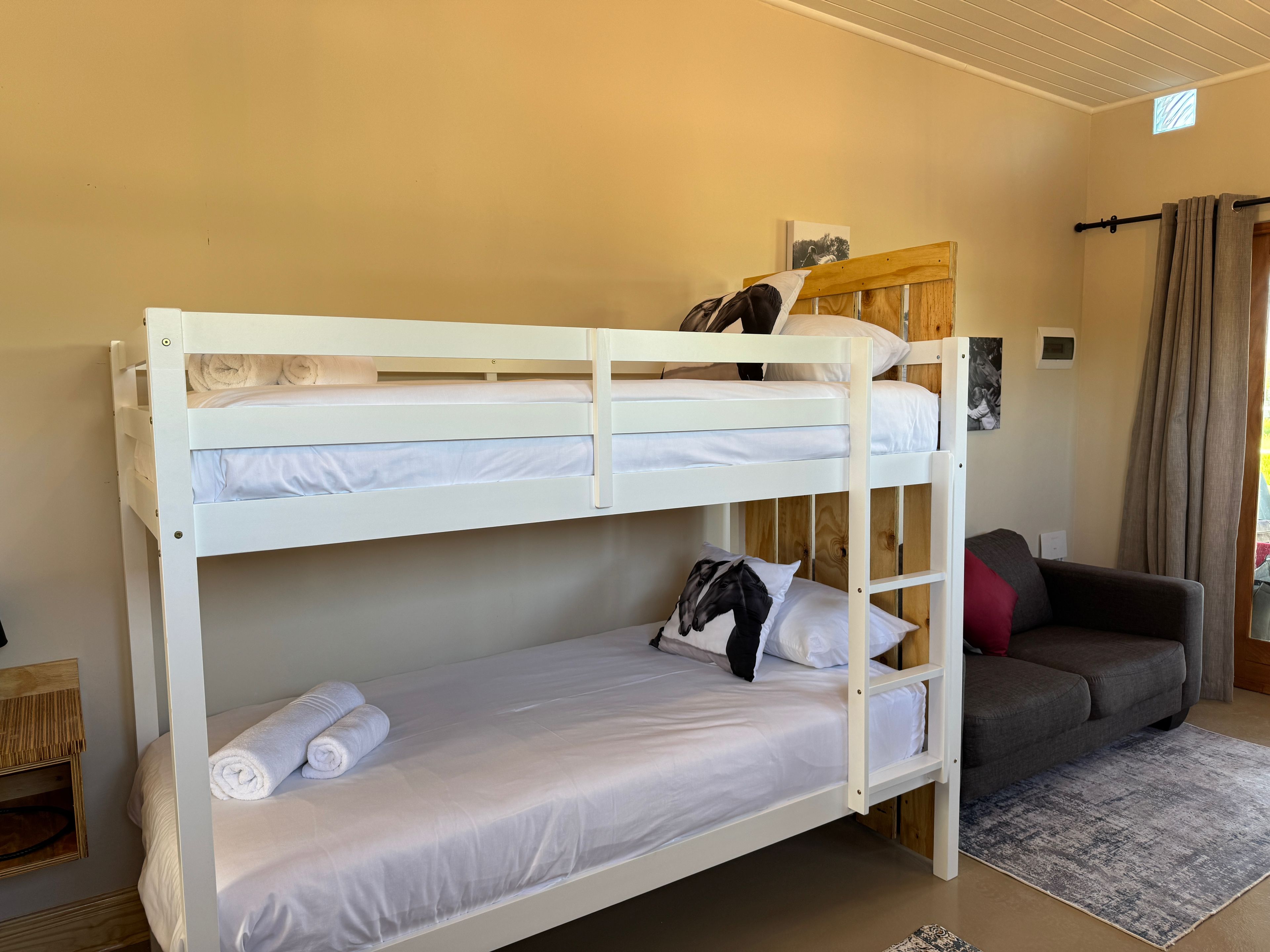 A bunk bed with white bedding, a grey sofa, and a small rug in a room with beige walls.