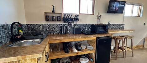 Una cocina compacta con un lavamanos, microondas y un refrigerador pequeño.