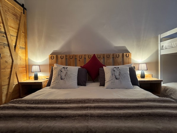 A bedroom with a wooden headboard, two bedside tables with lamps, a bed with a fluffy blanket, and a red pillow.