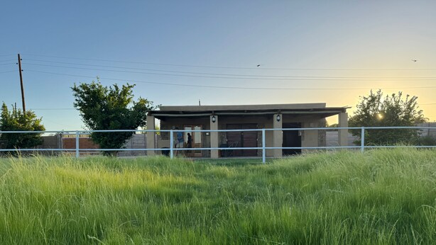 Un edificio con zona cercada, un campo de césped al frente y un cielo despejado.