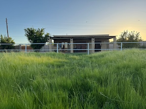 A building with a fenced area, a grassy field in the foreground, and a clear sky.