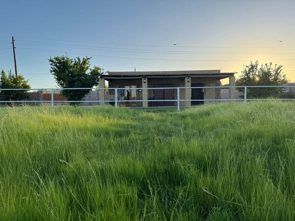 A building with a fenced area, a grassy field in the foreground, and a clear sky.