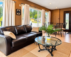 A living room with a leather sofa, a glass coffee table, and a dining area with chairs and a table.