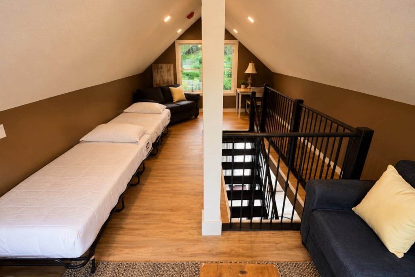 A dormitory room with bunk beds, a sofa, a small table, and a staircase.