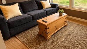 A modern living room with a dark sofa, a wooden coffee table, and a large window offering a view of a residential area. - Beaver Creek Chalet | 1 Bedroom | Sleeps 6 | Pet Friendly (Alberni-Clayoquot)