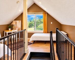 A bedroom with a bed, a desk, a chair, a window with curtains, and a view of greenery.