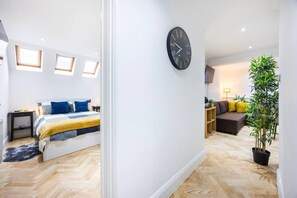 A modern bedroom with a bed, bedside tables, and a large window. - West Kensington 2BR | Steps to Tube | Sleeps 7 (Greater London)