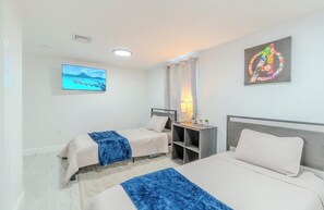 Habitación de hotel con dos camas, televisión, un cuadro y una mesita de noche con lámpara.