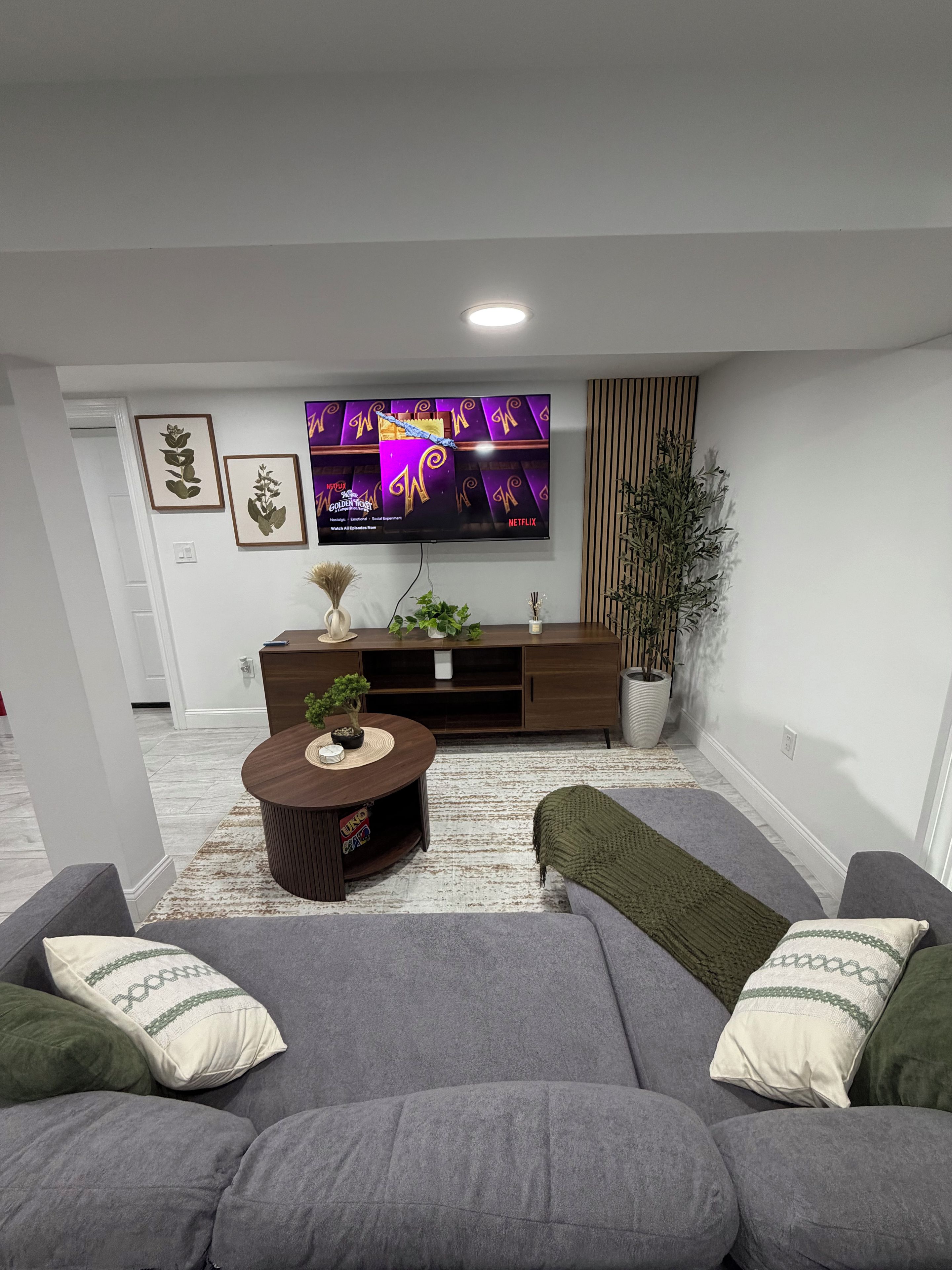 Un salon moderne avec un téléviseur à écran plat, une table basse en bois et un canapé gris agrémenté de coussins décoratifs.