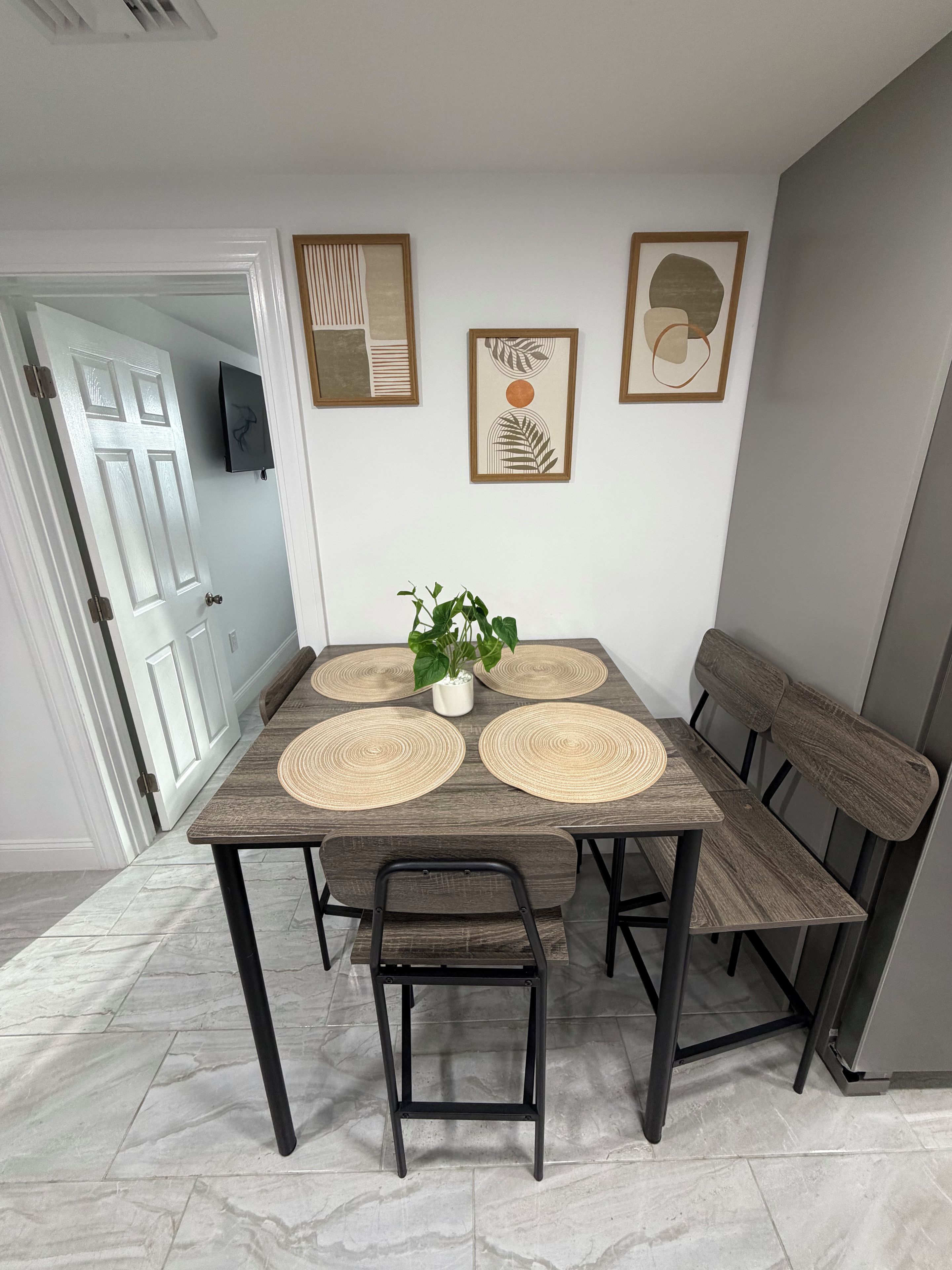 Un coin repas avec une table en bois, quatre sets de table en fibres tressées, une plante en pot et un banc.