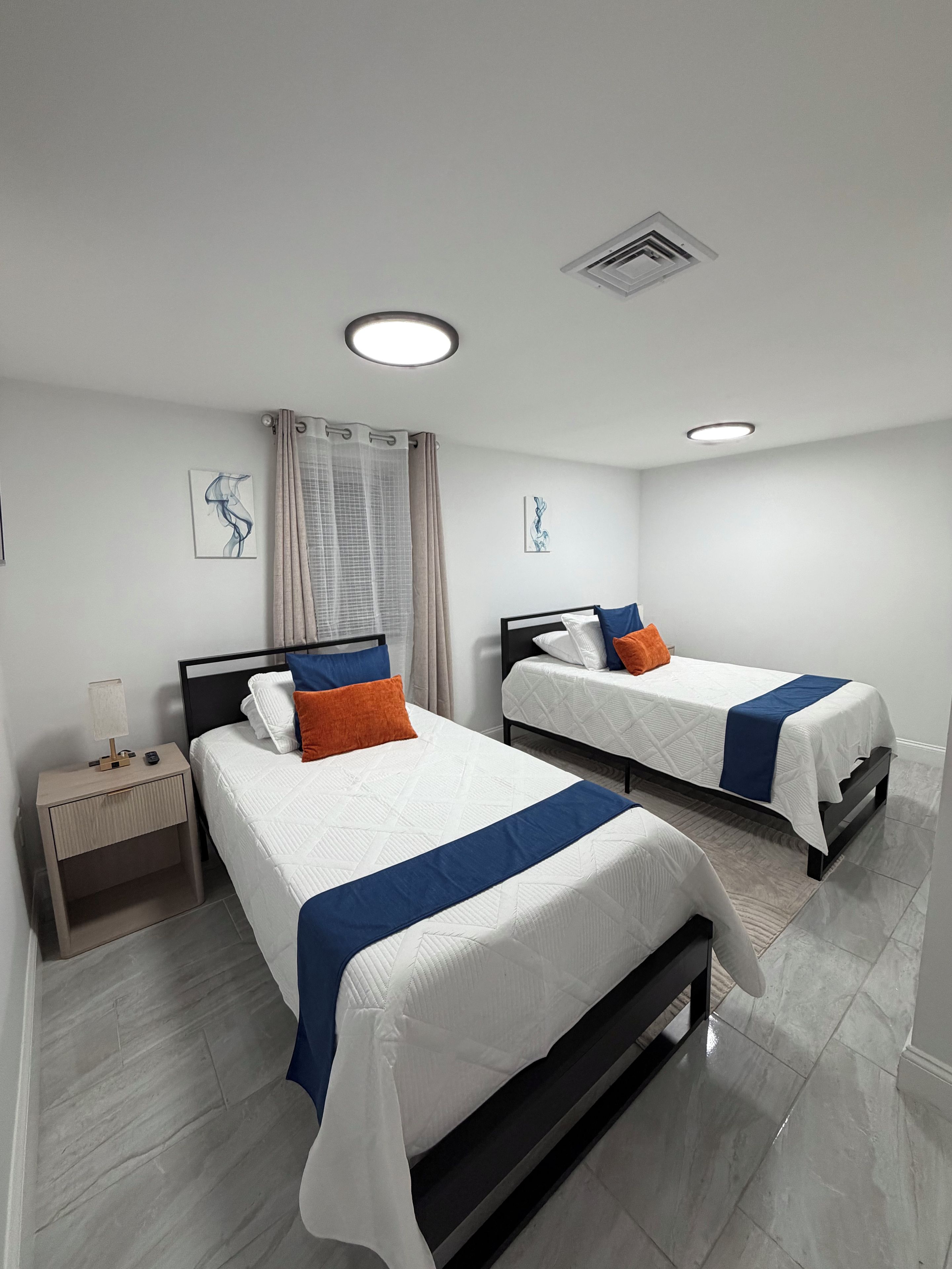 Une chambre d’hôtel avec deux lits, une table de chevet et une fenêtre avec des rideaux.