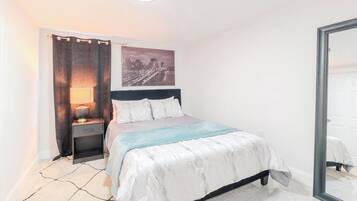 Een slaapkamer met een bed, nachtkastje, lamp en een stadsgezichtschilderij aan de muur.