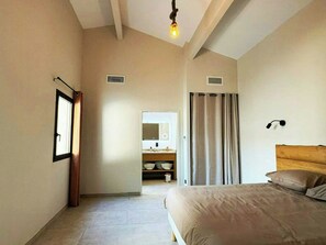 Ein Schlafzimmer mit einem Bett, einem Nachttisch, einem Spiegel, einem Fenster und einer Tür zu einem Badezimmer.
