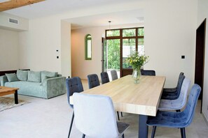 Ein Essbereich mit einem Holztisch und Stühlen, einem Sofa und einem Fenster mit Blick auf Bäume.