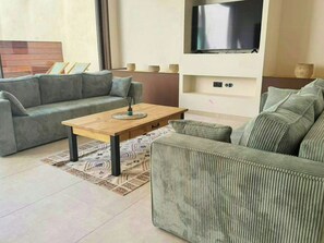 Un salon moderne avec un ensemble de canapés, une table basse et un téléviseur à écran plat fixé au mur.