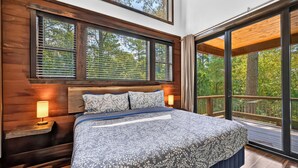 A bedroom with a large bed, wooden headboard, and multiple windows. - Games | Gallery Vibes | Hot Tub | Sleeps 14 (Broken Bow)