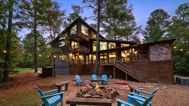 A two-story wooden cabin with a stone exterior, a deck, and outdoor seating. - Games | Gallery Vibes | Hot Tub | Sleeps 14 (Broken Bow)