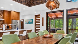 A modern kitchen with wooden cabinets, a stainless steel refrigerator, and a dining area with a wooden table and green chairs. - Games | Gallery Vibes | Hot Tub | Sleeps 14 (Broken Bow)