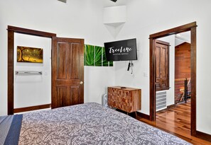Quarto com cama, TV, guarda-roupa de madeira e porta que dá para uma escadaria.