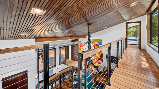 Un intérieur spacieux avec un plafond haut, des poutres en bois et une mezzanine dotée d’une rambarde.