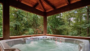 A hot tub with a wooden roof and a view of a forest. - Games | Gallery Vibes | Hot Tub | Sleeps 14 (Broken Bow)