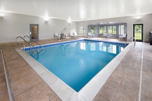 An indoor swimming pool with clear blue water, surrounded by tiled flooring and white walls.
