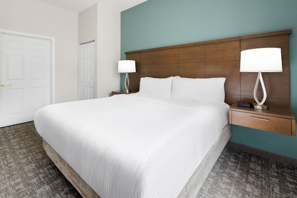 A hotel room with a large bed, two bedside tables, a door, and a wall with a wooden headboard.