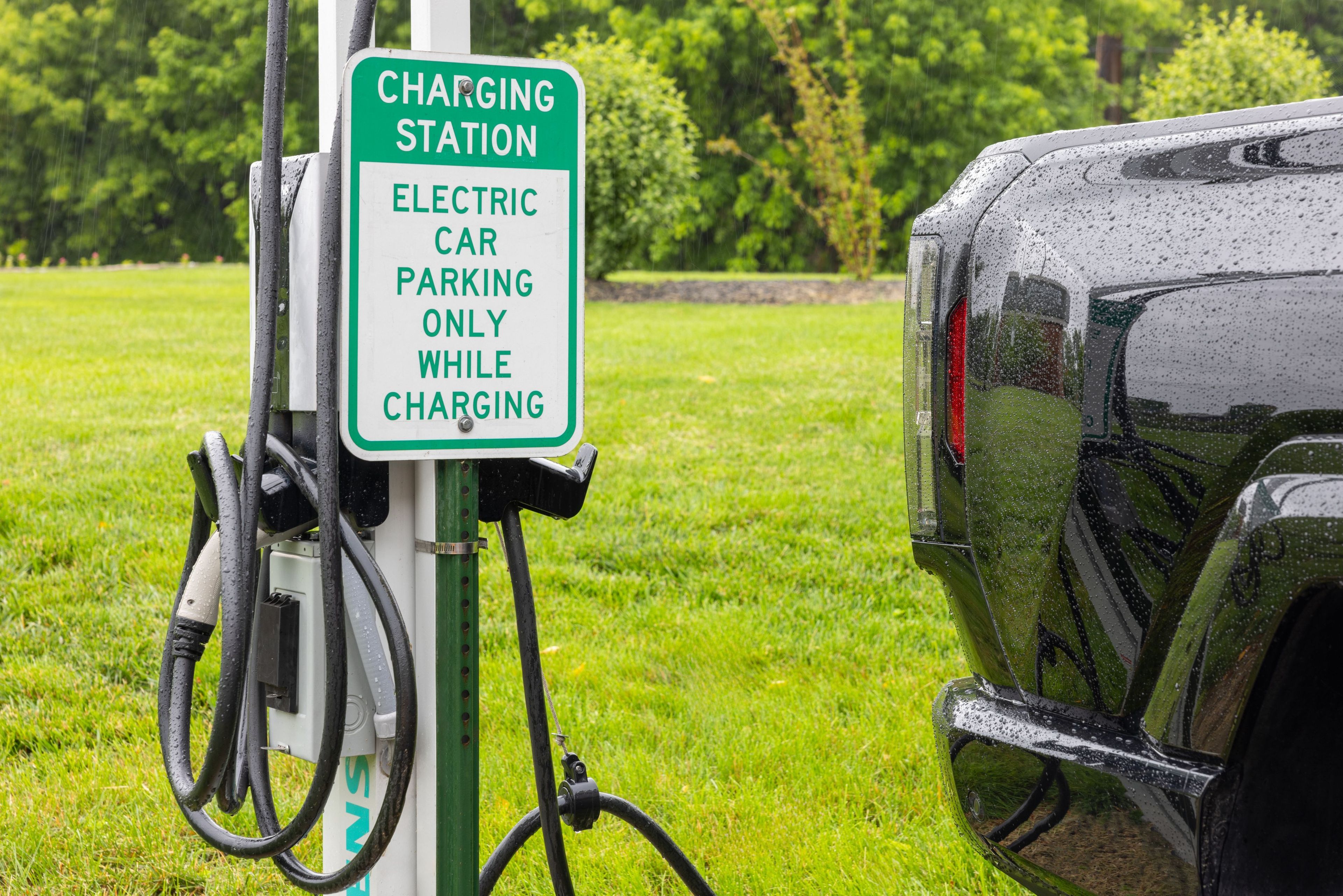 A charging station sign for electric cars in a grassy area.