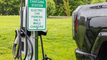 A charging station sign for electric cars in a grassy area.