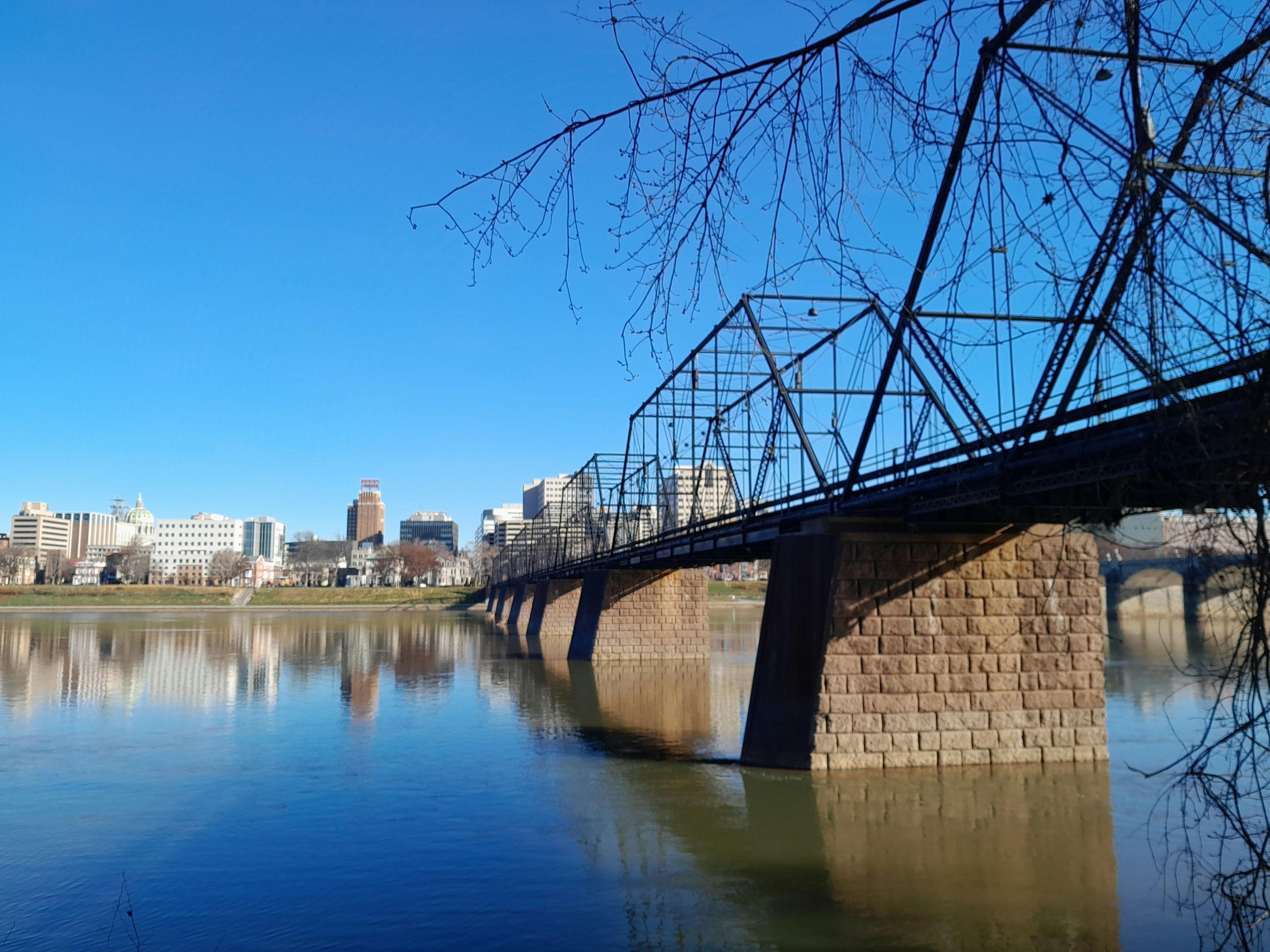 Eine Brücke über einem ruhigen Fluss, im Hintergrund eine Stadtlandschaft.