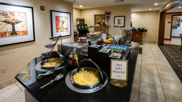 Disposição de buffet com diversos alimentos e placa indicando café da manhã diário gratuito.