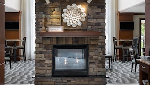 Uma lareira de pedra com uma peça floral decorativa acima, um letreiro com a frase 'HOMESWEET home' e uma TV de tela plana fixada na parede.