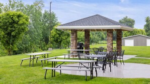 Área de terraço ao ar livre com mesas de piquenique e um gazebo.