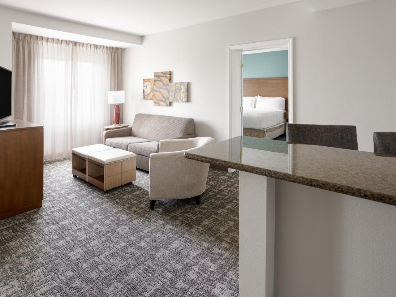 A hotel room with a bed, a sofa, a small table, a TV, and a window with curtains.