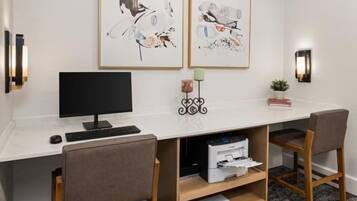 A modern office space with a desk, two chairs, a computer, and framed artwork on the wall.