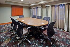 A conference room with a large wooden table surrounded by chairs, a carpeted floor, and curtains on the windows.