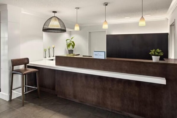 A reception desk with a dark wood finish, pendant lighting, and a potted plant.